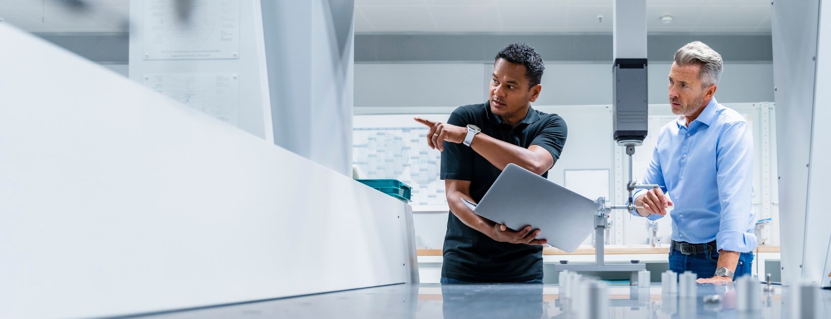 Engenheiro com laptop apontando para empresário em uma fábrica.